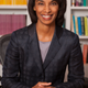 Labor economist and Princeton dean Cecilia Rouse smiles and sits at at desk in front of bookcases in a black blazer.
